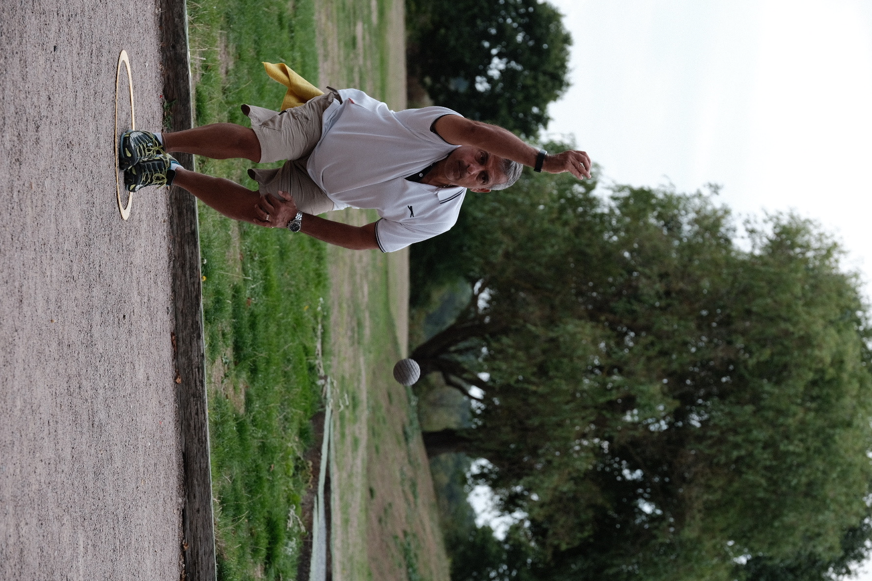 A crouching man throws a metal boule on a pétanque piste.